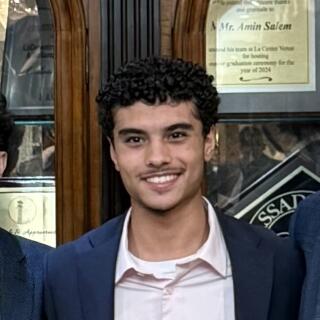 A smiling man in a white shirt and a blue jacket