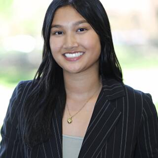 A smiling woman in a grey shirt and dark striped jacket