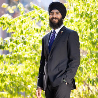 A smiling person in a dastar and a dark suit