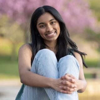 A smiling woman in jeans sits hugging her legs