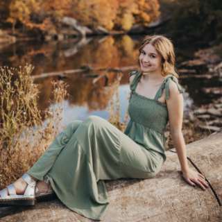 A person in a green dress sits outside next to a pond
