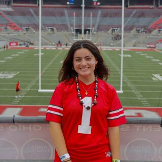 A smiling person in an Ohio State jersey in front of a football field