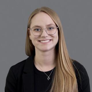 A smiling person with glasses in a black shirt and jacket