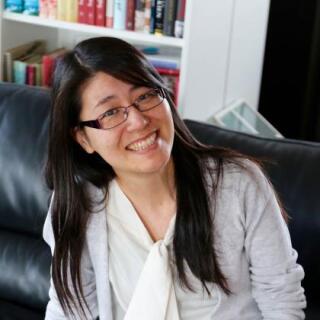 A smiling person in a white shirt, grey sweater and glasses