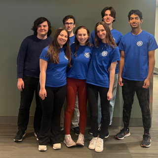 A group of smiling people in blue shirts stands together