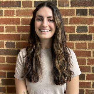 Photo of a white woman with brown curly hair and a tan shirt smiling