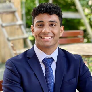 A smiling person in a blue shirt, jacket and tie