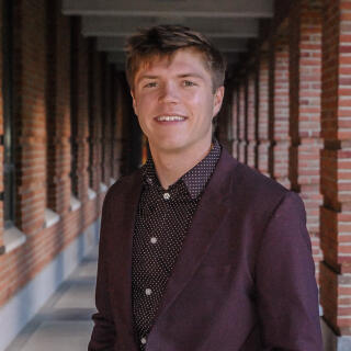 A smiling man in a maroon shirt and jacket