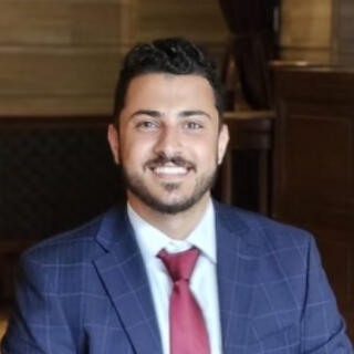A smiling person in a white shirt, blue jacket and red tie