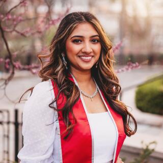 A smiling woman in a white dress wearing a red graduation stole