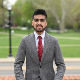 A smiling man in a white shirt, grey jacket and red tie with a Block O lapel pin