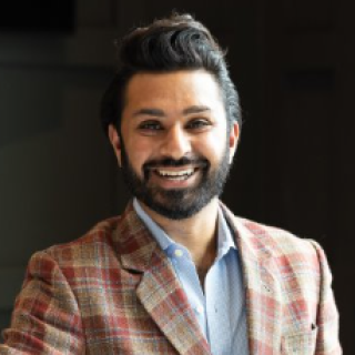 A smiling man in a blue shirt and a red and brown plain jacket