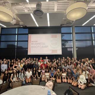 A group of smiling people stand together before a projector reading "Business Bootcamp"