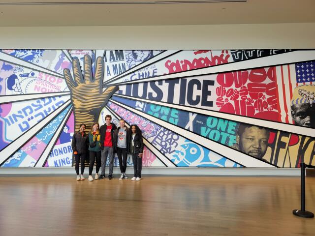 Group of 5 college students posing in front of colorful mural at museum