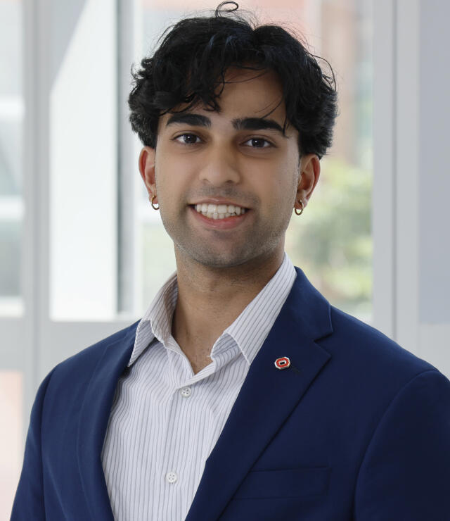 An image of Alexander Abreo. He has brown hair and brown eyes, and wears a navy blue suit with a blue button down shirt.