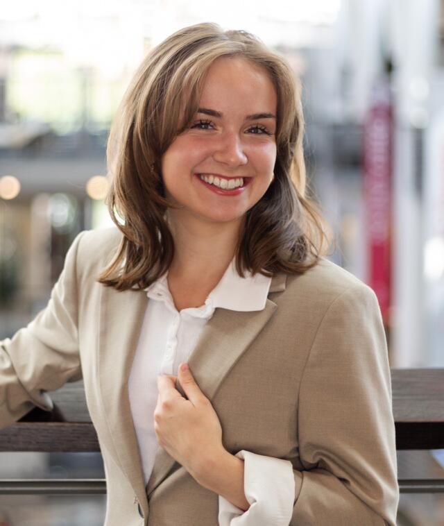 An image of Ally Lewis. She has blonde hair and blue eyes, and wears a white blazer.