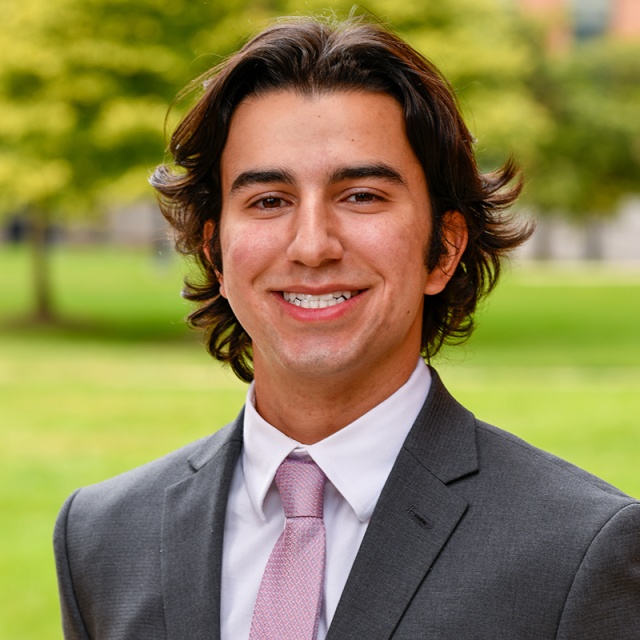 A headshot image of Cameron Shahrooz. He has brown hair and brown eyes and wears a black suit with a red tie.