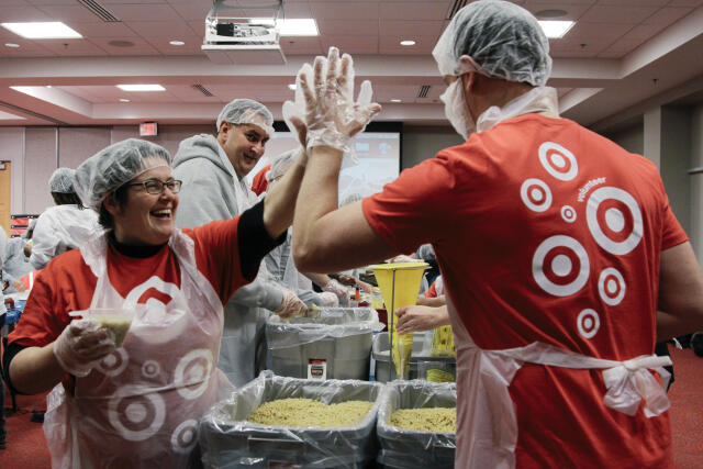 Two volunteers in hairnets and aprons high fiving while preparing and packaging food together