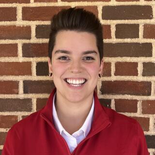 photo of a white person smiling wearing a red pullover and white collared shirt