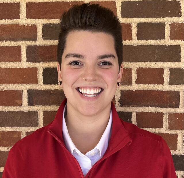 photo of a white person smiling wearing a red pullover and white collared shirt