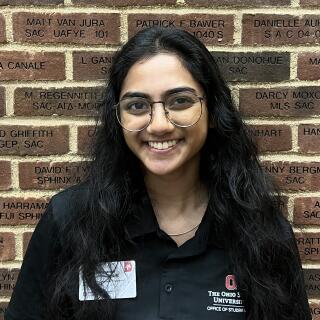 photo of a smiling woman with long black hair and glasses wearing a black polo