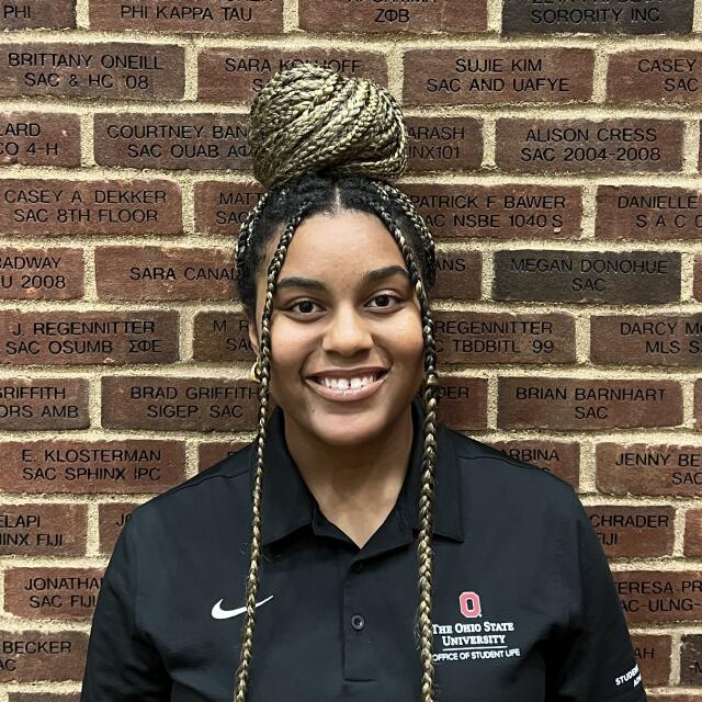 photo of a smiling woman with long black and blonde hair in braids wearing a black polo