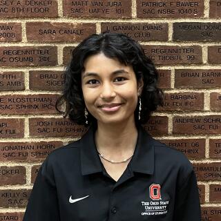 photo of a smiling woman with shoulder length black curly hair wearing a black polo