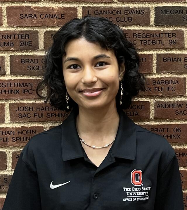 photo of a smiling woman with shoulder length black curly hair wearing a black polo