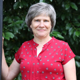 Photo of a white woman with a gray bob and a red shirt