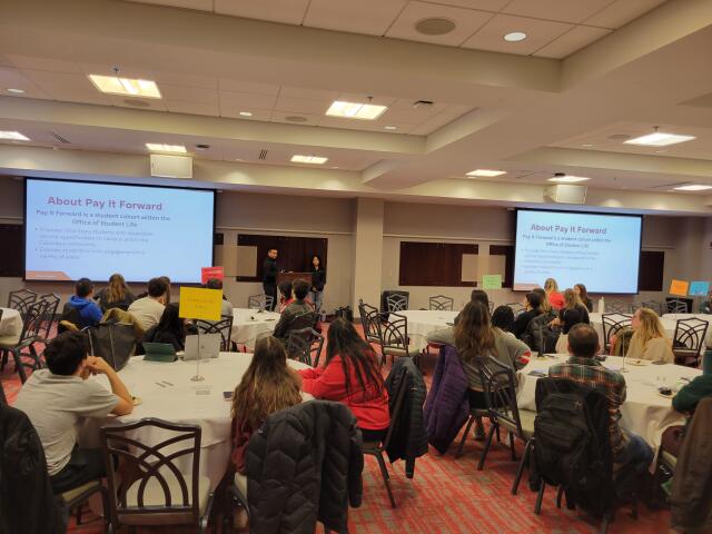 Students seated at round banquet-style tables at Pay It Forward presentation