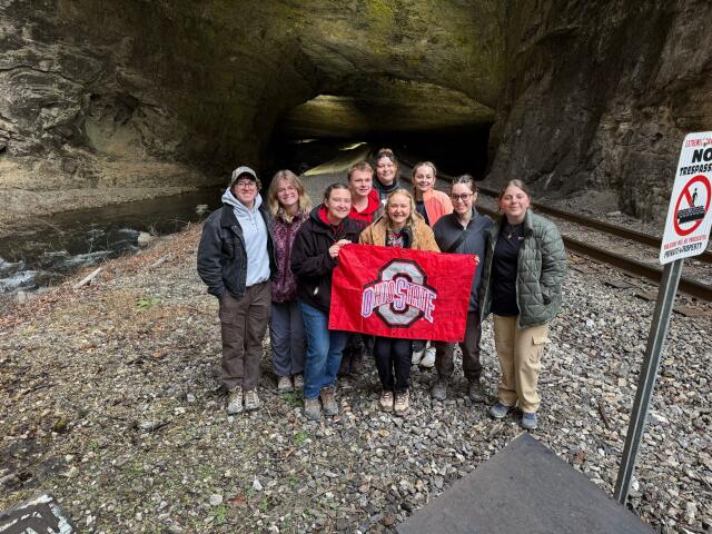 The 2026 group poses with an Ohio State Flag at the entrance of the Natural Tunnel