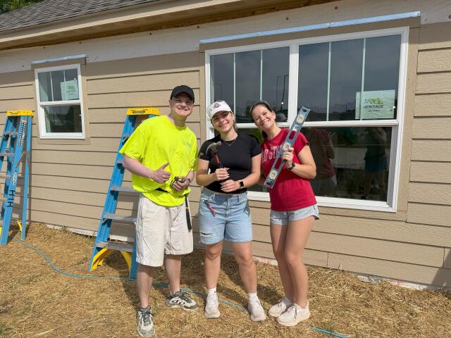 Three students holding tools while working to build a home with Habitat for Humanity