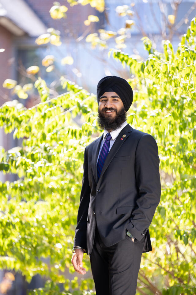 A smiling person in a dastar and a dark suit
