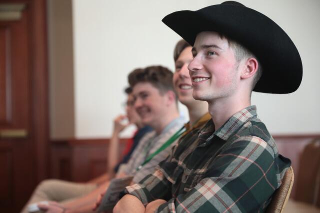 A smiling person in profile wearing a plaid shirt and a cowboy hat