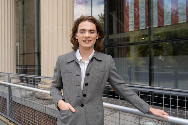 A smiling person in a white shirt and grey jacket