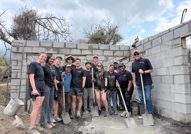 11 Buck-I-SERV participants stand in front of a house with shovels in Antigua, Guatemala