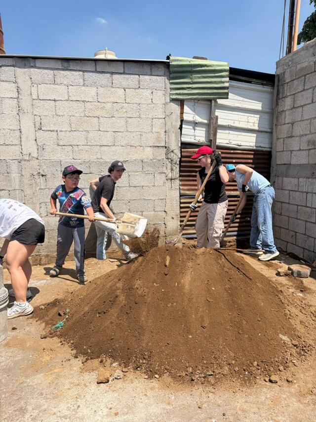 Students work with community members to shovel dirt and build a home