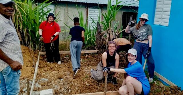 Volunteers pause for a photo while clearing land and leveling ground to build a new structure