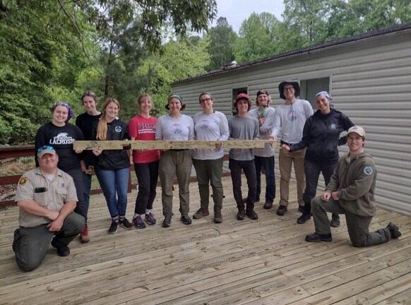 College students holding a long plank of wood and posing alongside park rangers