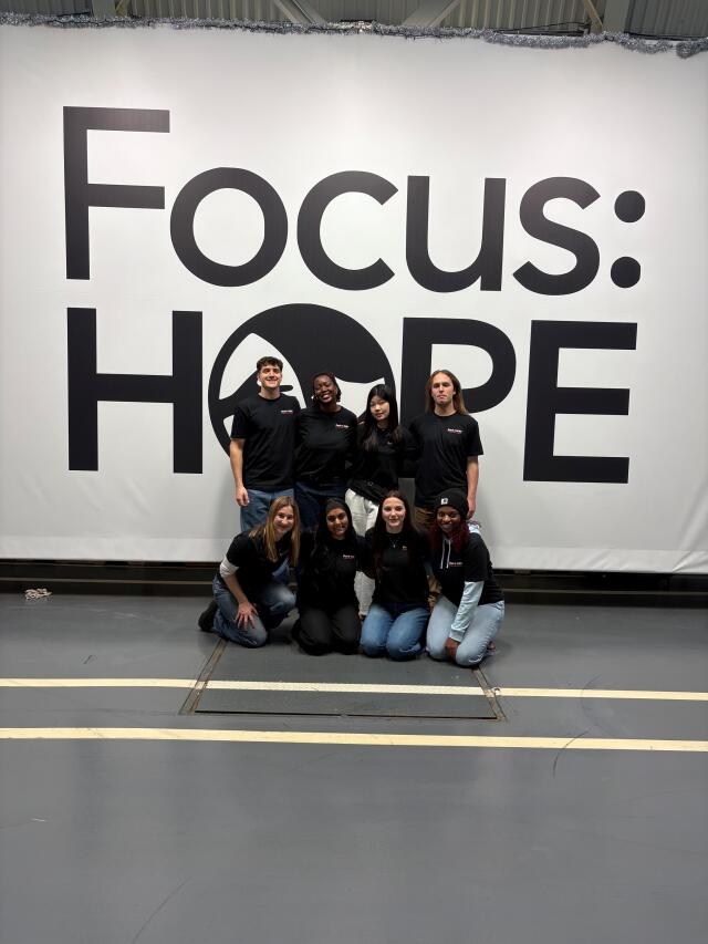 A group of 8 from Ohio State stand in front of a Focus: Hope sign while volunteering.