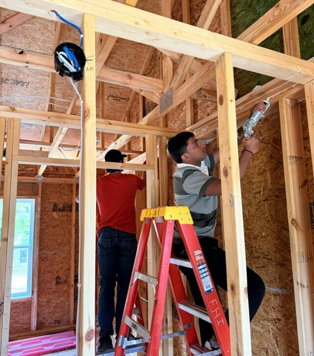 Students stand on ladders and work to caulk and seal the interior of a home