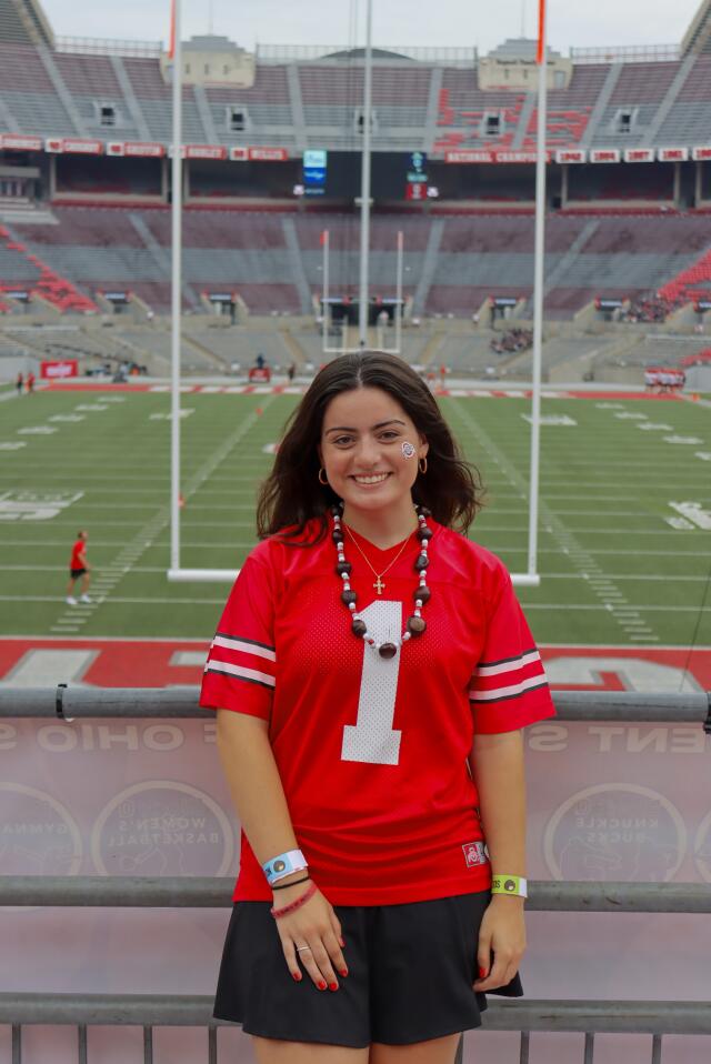 A smiling person in an Ohio State jersey in front of a football field