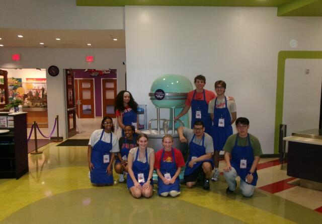 Group picture of 9 volunteers in front of a cotton candy machine at Give Kids the World in Florida