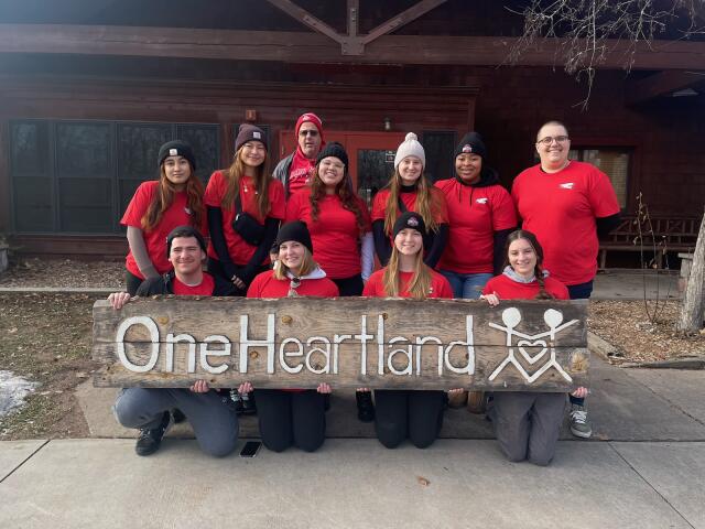 11 volunteers wearing red shirts holding One Heartland sign