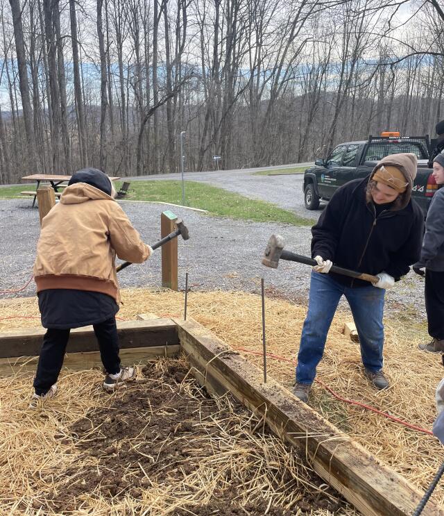 Two students hammer steaks into the ground to secure a new park structure at the State Park