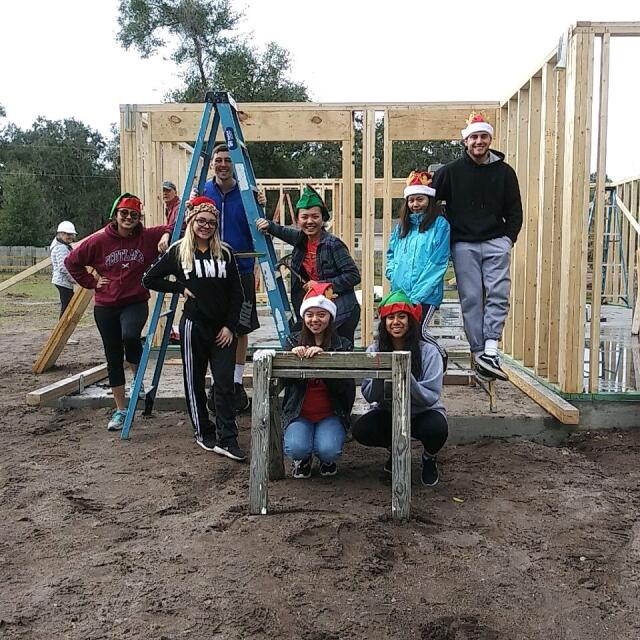 Group of college students posing in front of frame of house they helped to construct