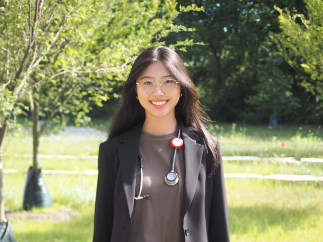A smiling woman in a black jacket with a stethoscope around her neck