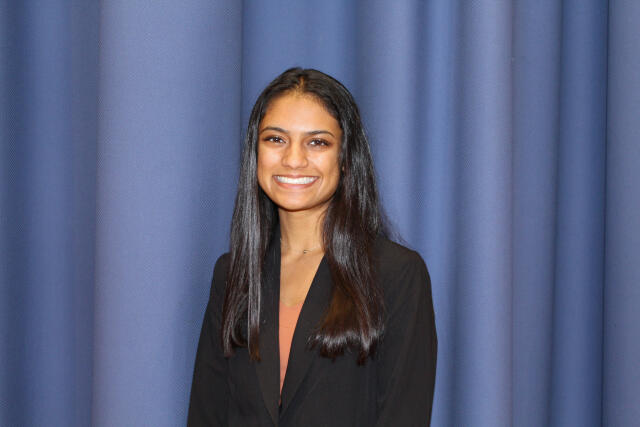 A smiling woman in an orange shirt and black jacket
