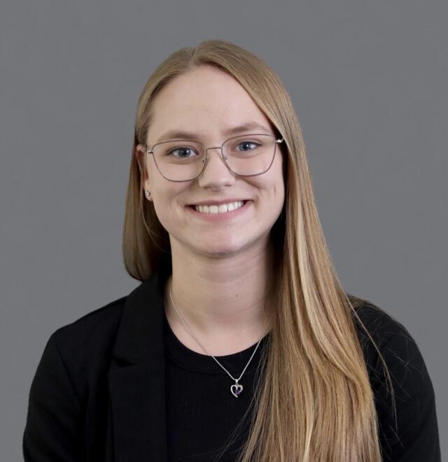 A smiling person with glasses in a black shirt and jacket