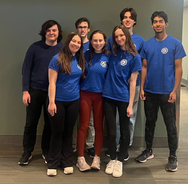 A group of smiling people in blue shirts stands together